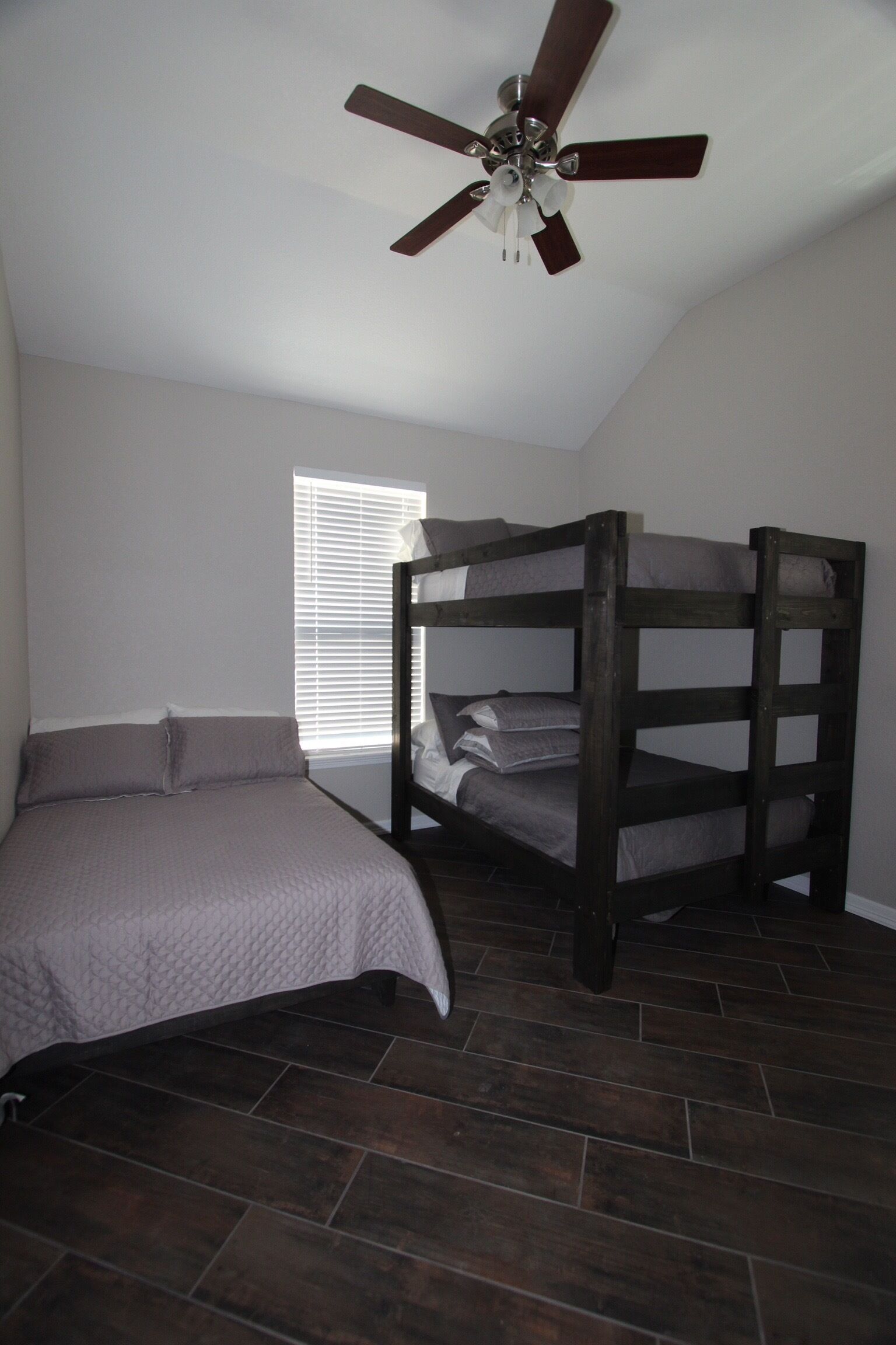 A bedroom with a bunk bed, a single bed, a ceiling fan, and a window with blinds.