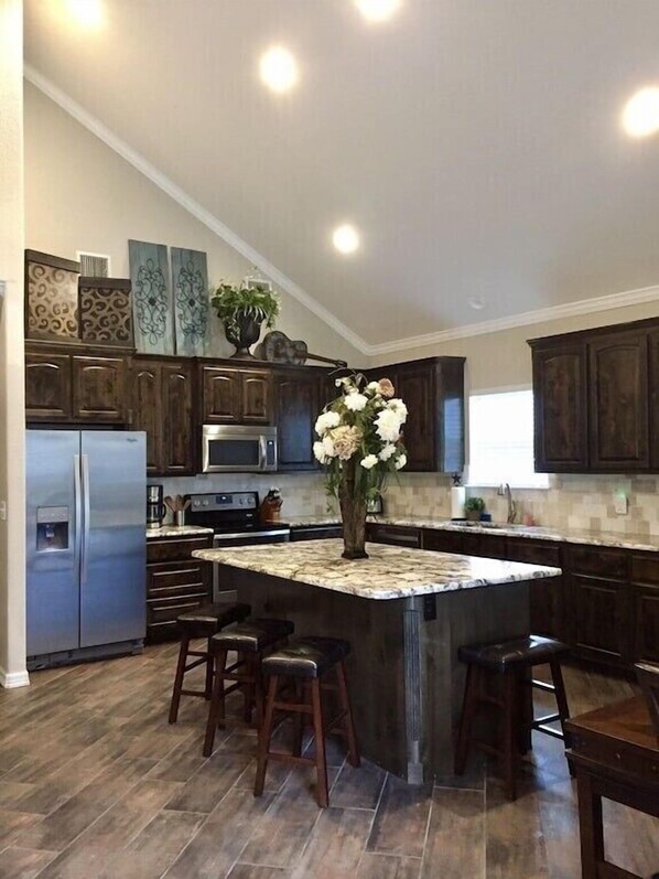 A modern kitchen with dark wood cabinets, a stainless steel refrigerator, a microwave, and a large island with bar stools.