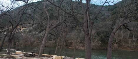 A riverside park with picnic tables and benches, surrounded by trees and hills.