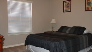 A bedroom with a bed, a nightstand, a lamp, and a window with blinds.