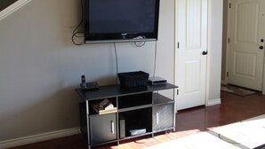 A room with a mounted TV on a wall, a small cabinet below it, and a white door.