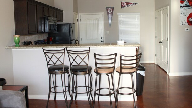 A kitchen with four bar stools, a refrigerator, and a microwave.