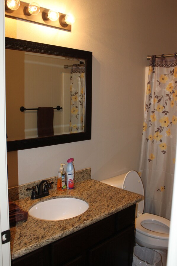 A bathroom with a granite countertop sink, a mirror with lights, a towel rack, and a shower curtain with a floral pattern. - Minutes from A&M (Bryan)
