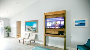 Ein modernes Wohnzimmer mit Wand-Fernseher, zwei Sesseln, einem blauen Teppich und gerahmten Kunstwerken an den Wänden.