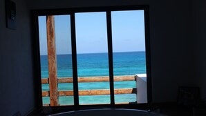 A room with a large window overlooking a wooden deck and the ocean. - Beautiful Oceanfront Mexican Villa with Infinity Pool, and Spectacular View (Isla Mujeres)