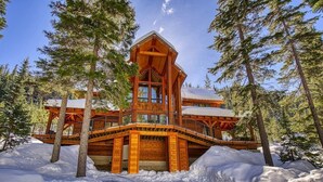 A wooden cabin with a balcony, surrounded by snow and trees.
