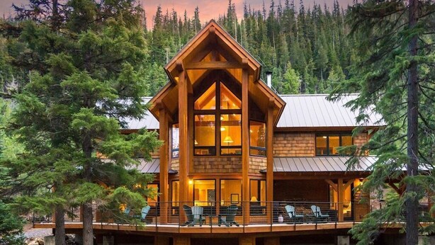 A log cabin with a large porch and multiple windows, surrounded by trees.