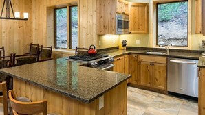 A wooden cabin-style kitchen with granite countertops, a central island, and a stainless steel dishwasher.