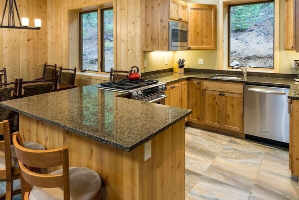 Una cocina tipo cabaña de madera con encimeras de granito, una isla central y un lavavajillas de acero inoxidable.
