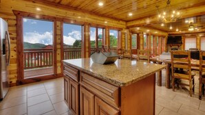 A wooden cabin interior with a kitchen area featuring a granite countertop, wooden cabinets, and a dining table with chairs. - A Heavenly View Too ~ 6 BR w/ Indoor Pool ~ Sleeps 28 ~ Incredible Views! (Sevierville)