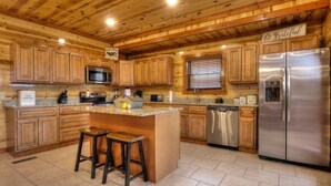 A kitchen with wooden cabinets, a stainless steel refrigerator, and a granite countertop. - A Heavenly View Too ~ 6 BR w/ Indoor Pool ~ Sleeps 28 ~ Incredible Views! (Sevierville)