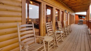 A wooden deck with wooden chairs and tables, large windows, and a view of the mountains. - A Heavenly View Too ~ 6 BR w/ Indoor Pool ~ Sleeps 28 ~ Incredible Views! (Sevierville)