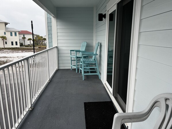 A covered porch with a black rubber mat, a white railing, and two turquoise chairs.