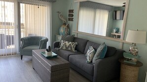 A living room with a sofa, armchair, and a coffee table. There is a mirror on the wall and a lamp on a side table. - Oceanfront condo, steps to beach & pool, across from Coligny Plaza! (Hilton Head)