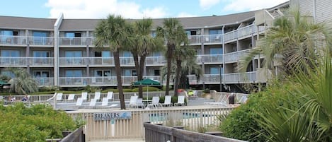 Un hotel de varios pisos con balcones, un área de piscina con tumbonas y una terraza de madera que da a la piscina.