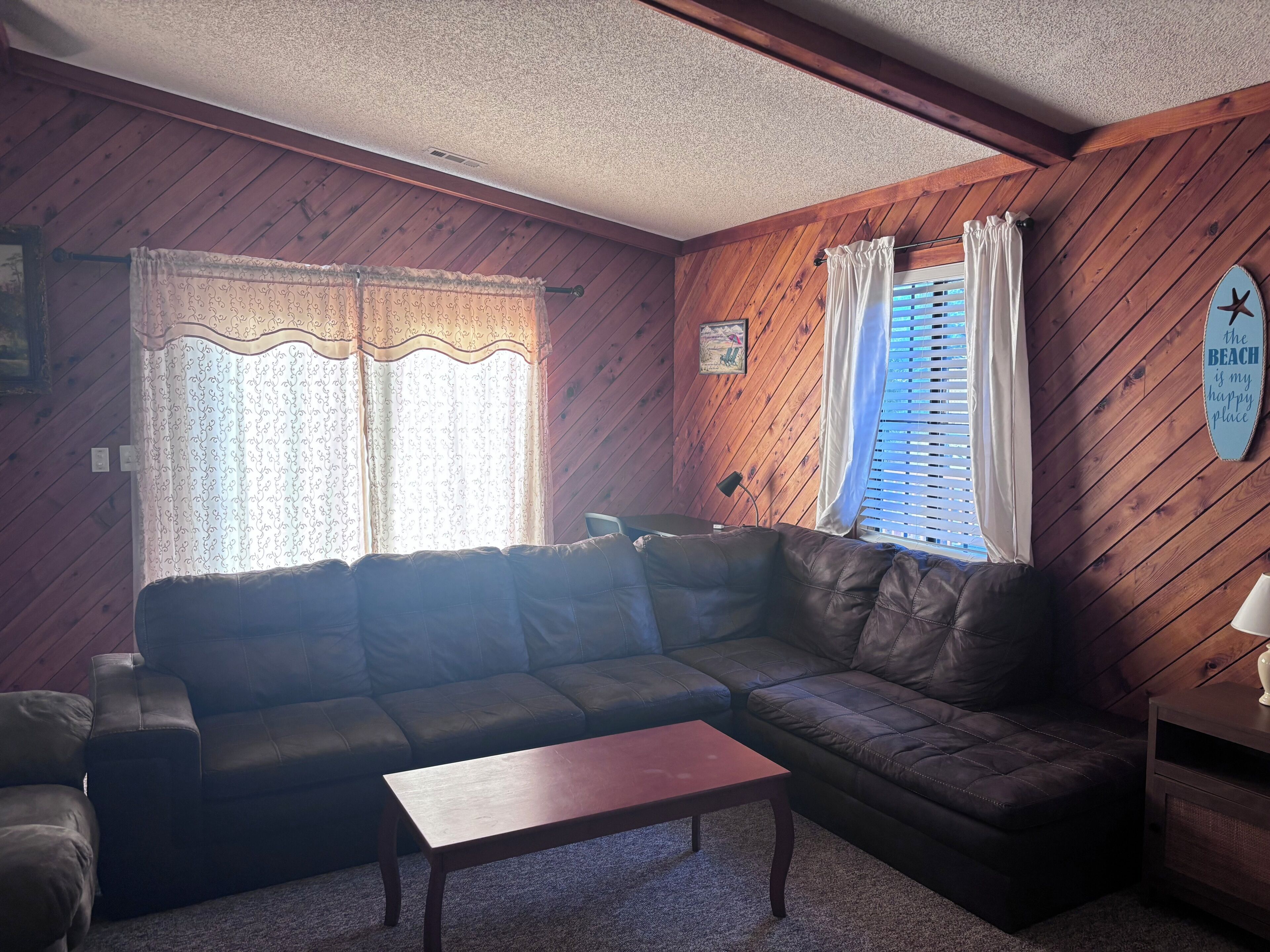 A living room with a dark leather sofa, a wooden coffee table, and a window with curtains.