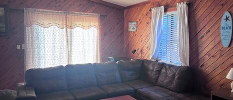 A living room with a dark leather sofa, a wooden coffee table, and a window with curtains.
