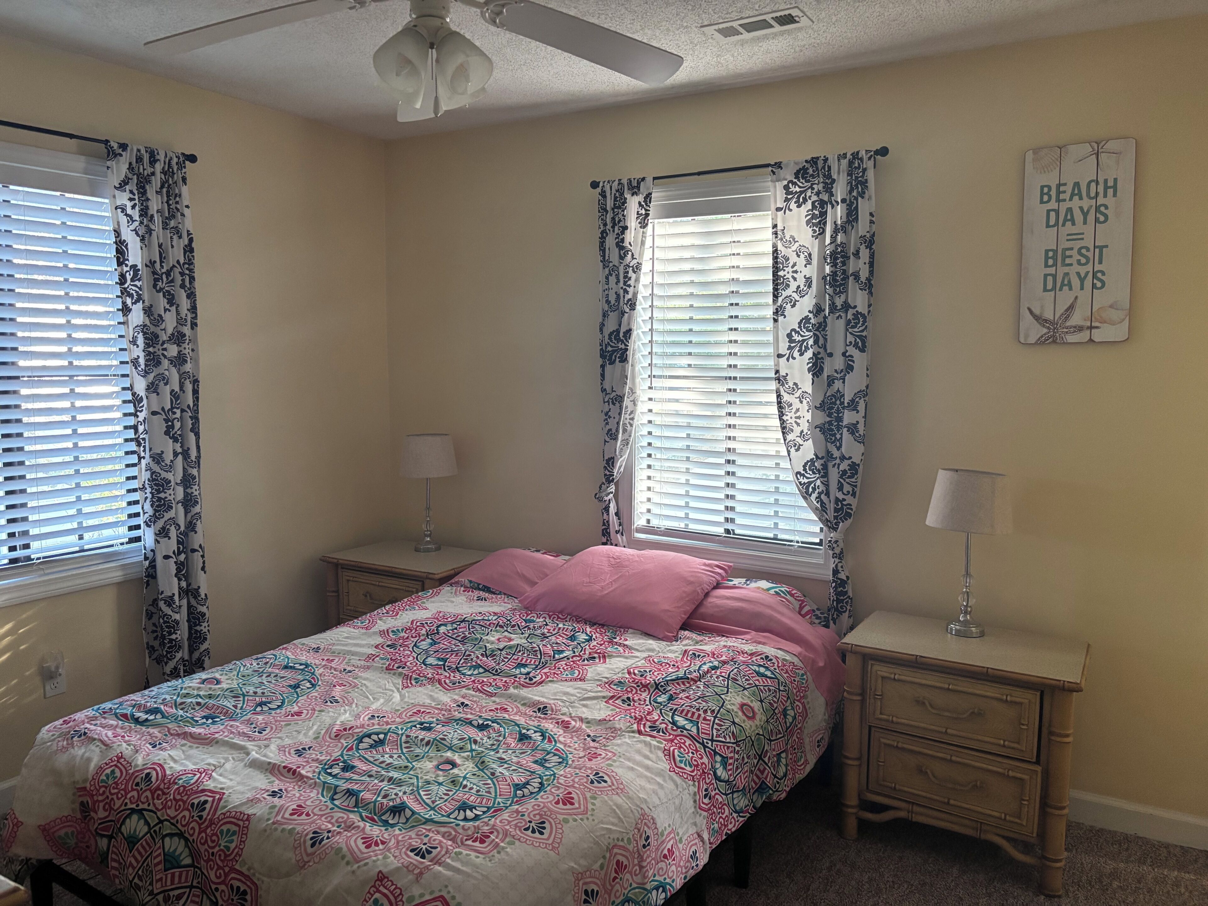 Une chambre à coucher comprenant un lit, deux tables de chevet, un ventilateur de plafond et un panneau décoratif mural.