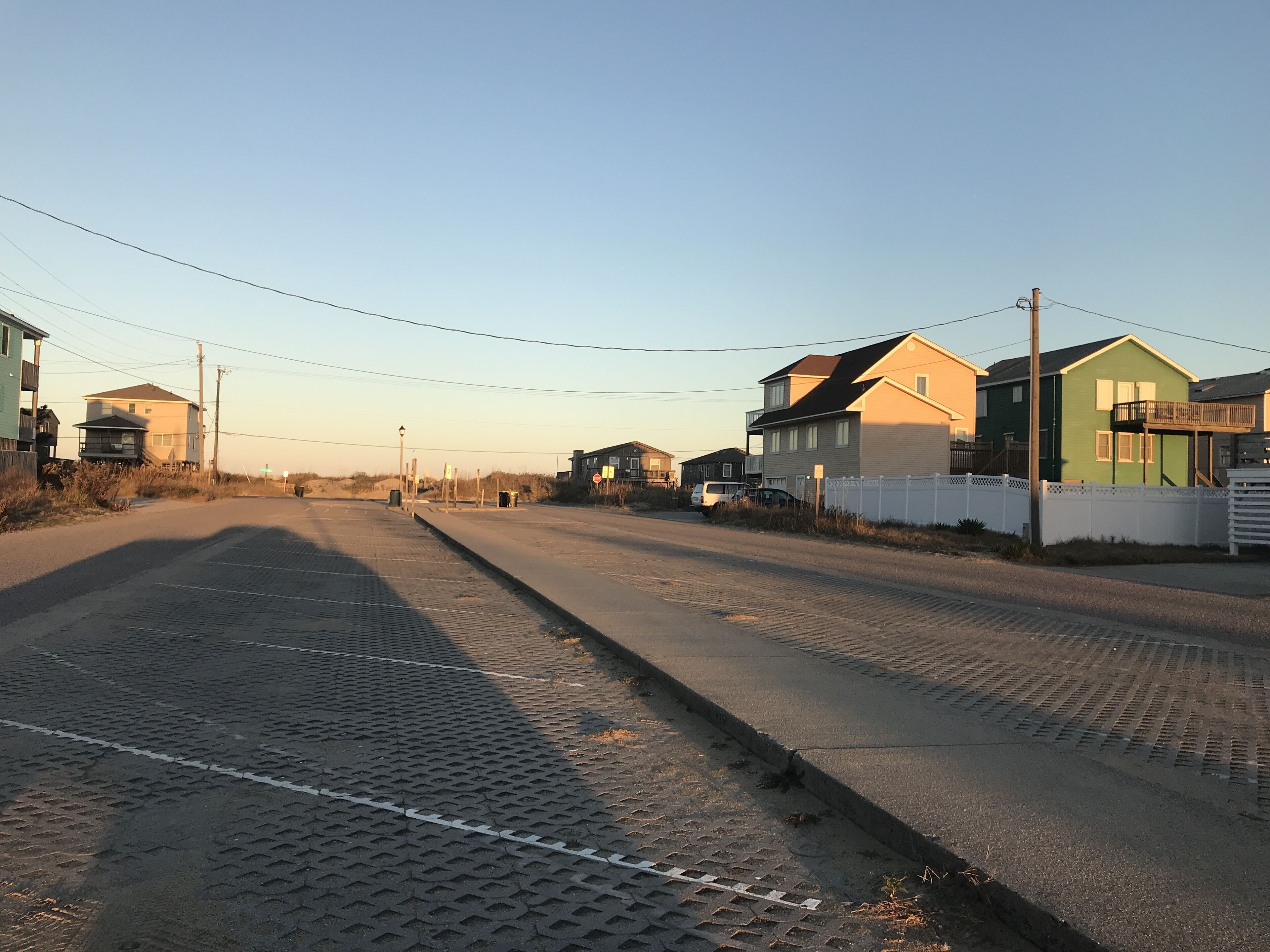 A residential street with houses on both sides, a clear sky, and a paved road with a curb.