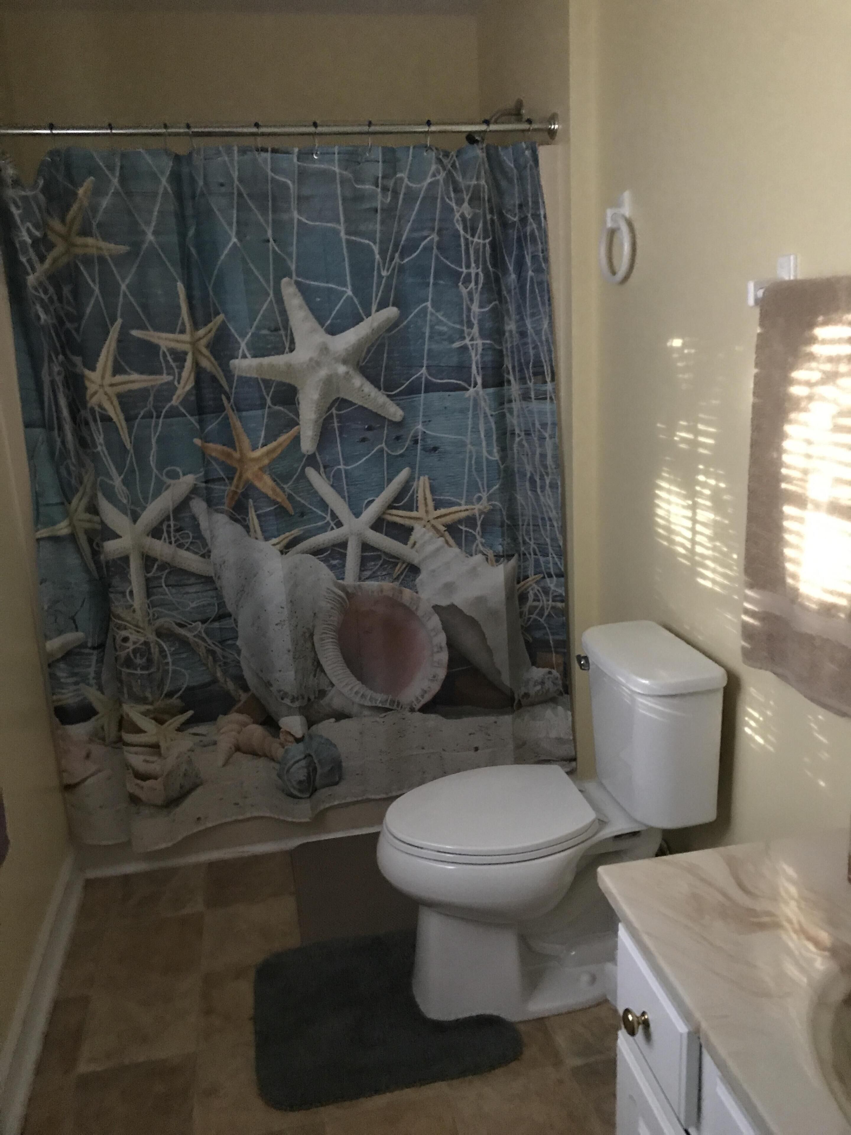 A bathroom with a shower curtain featuring starfish and shells, a toilet, and a sink with a marble countertop.
