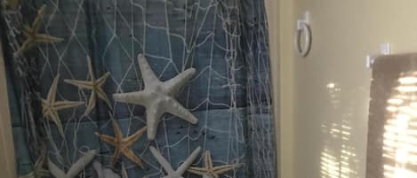 A bathroom with a shower curtain featuring starfish and shells, a toilet, and a sink with a marble countertop.