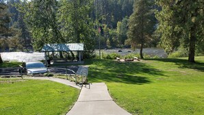 A park with a paved walkway, picnic tables, and a gazebo by a lake.