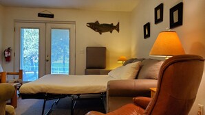 A hotel room with a bed, a sofa, a chair, a lamp, and a fish decoration on the wall.