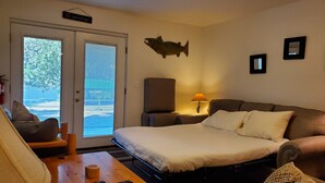 A hotel room with a bed, a sofa, a chair, a lamp, and a fish decoration on the wall.