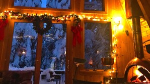A cozy cabin interior with a fireplace, wooden walls, and a view of a snowy landscape through large windows. - Cabin & Spa - Luxurious & Private 2 blocks from the lake and conservancy  (Tahoe City)