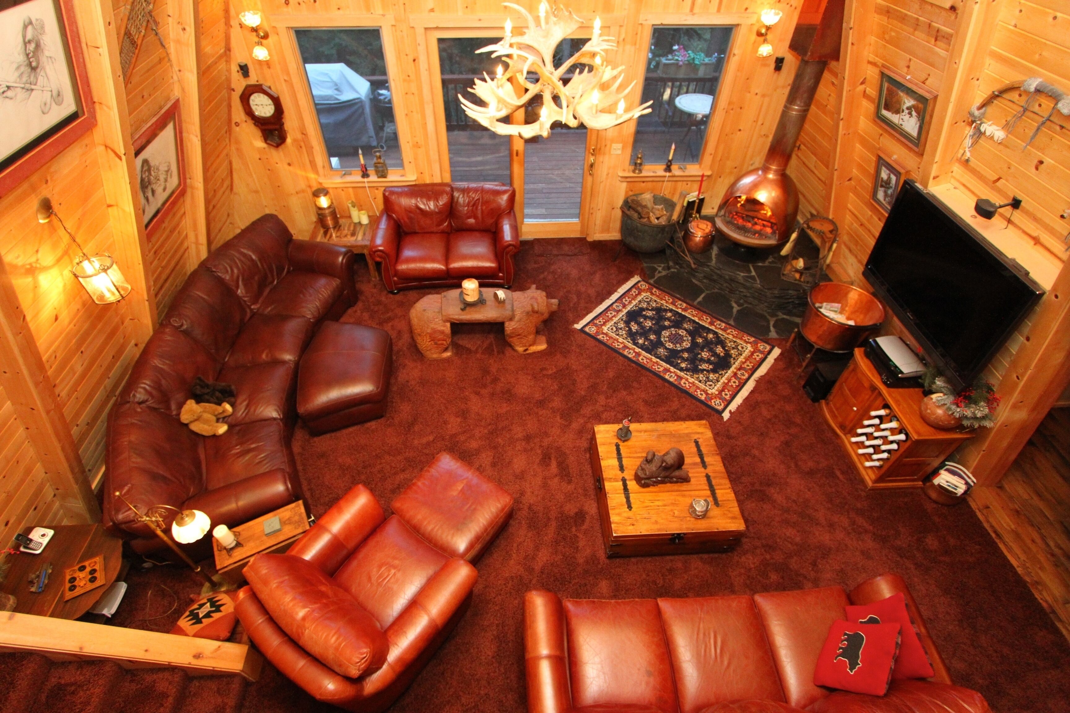 Un acogedor interior de cabaña de madera con un sofá de cuero, chimenea, televisor y un marco de piedra para la chimenea.