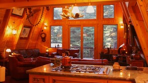 A cozy cabin interior with a fireplace, wooden walls, and large windows offering a forest view. - Cabin & Spa - Luxurious & Private 2 blocks from the lake and conservancy  (Tahoe City)