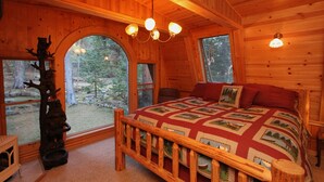A cozy log cabin bedroom with a large bed, wooden walls, and a view of the forest. - Cabin & Spa - Luxurious & Private 2 blocks from the lake and conservancy  (Tahoe City)