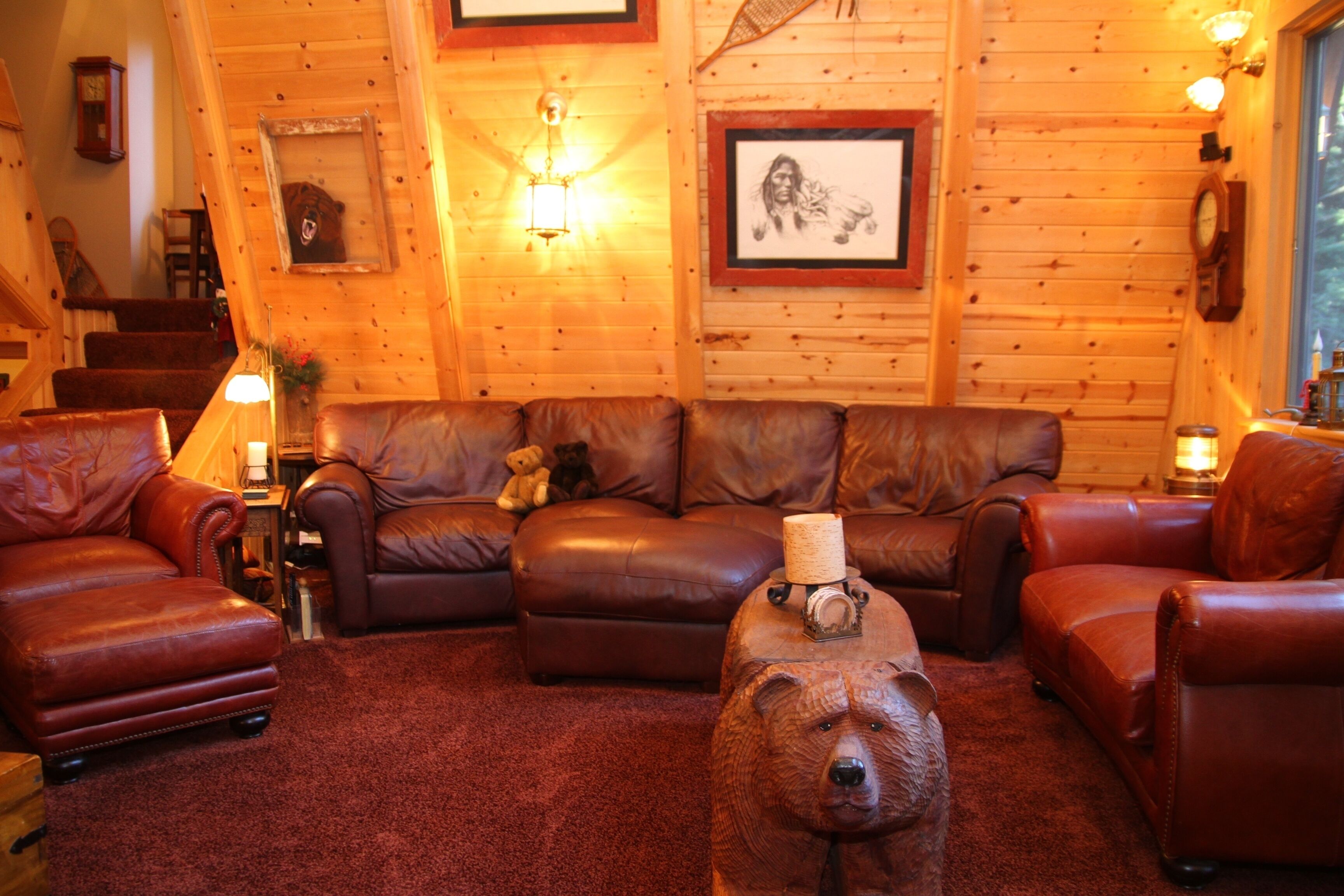 Een gezellig interieur van een blokhut met een bruine leren bank, twee leren fauteuils en een grote beerbeeld in het midden.