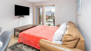 Un dormitorio con cama, televisor, escritorio y ventana con vistas a montañas.
