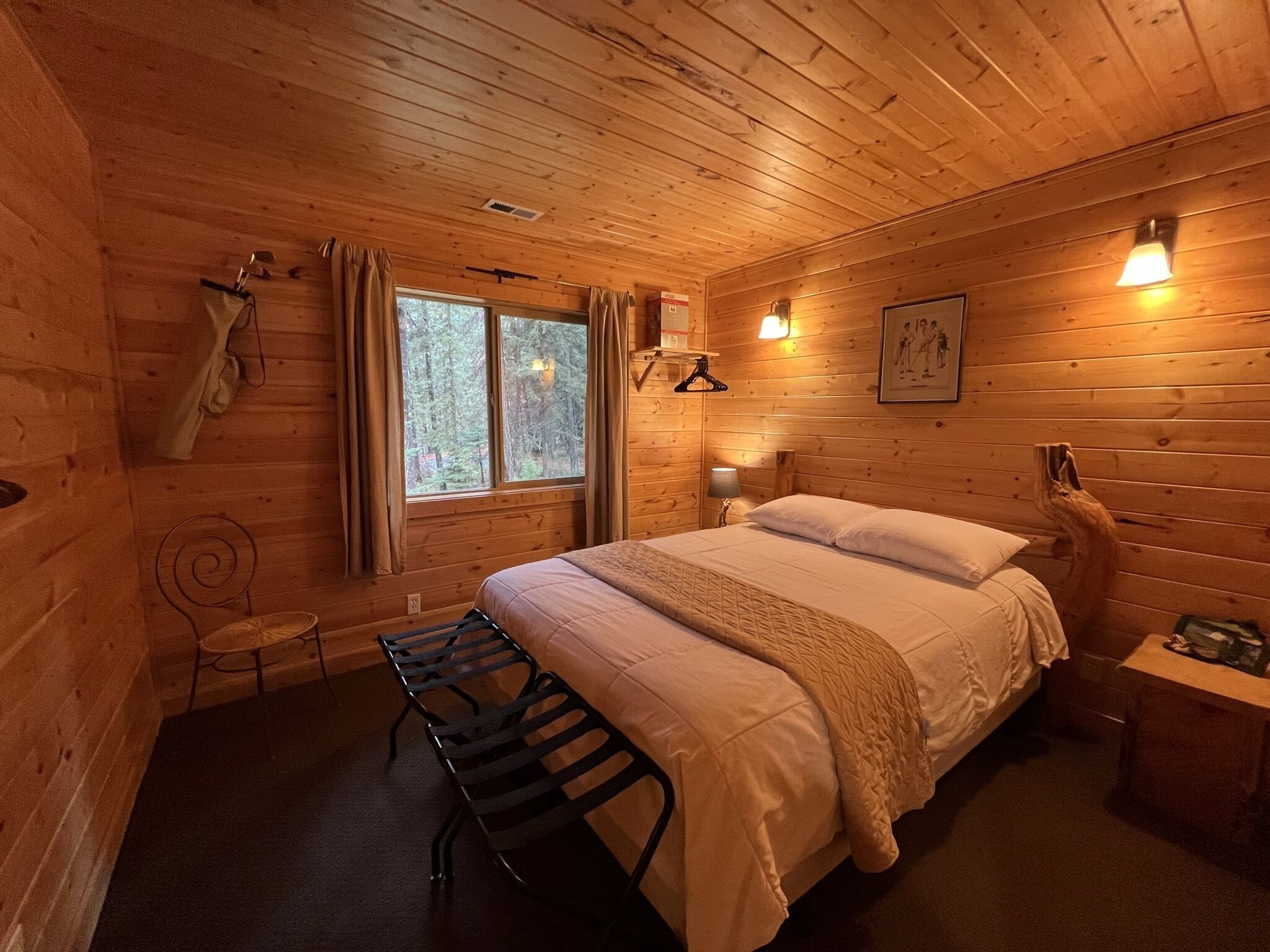 Een houten slaapkamer met een bed, een stoel, een nachtkastje, een lamp en een raam met gordijnen.