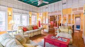 A spacious living room with a high ceiling, a ceiling fan, and a red coffee table. There are multiple seating areas with striped sofas and a dining table. - 'Roger's Lighthouse' in the Heart of Seaside. Bikes included.  (seaside)