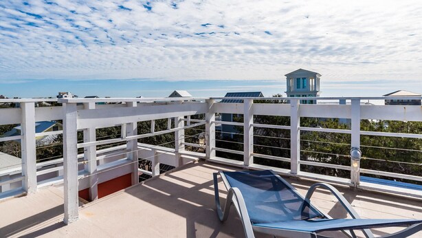A rooftop terrace with a blue lounge chair, white railings, and a view of the ocean and buildings. - 'Roger's Lighthouse' in the Heart of Seaside. Bikes included.  (seaside)
