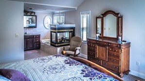 Een slaapkamer met een groot bed, een dressoir, een stoel, een open haard en een spiegel.