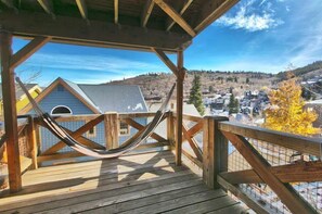 Una terraza de madera con una hamaca, con vista a un pueblo con casas y colinas.