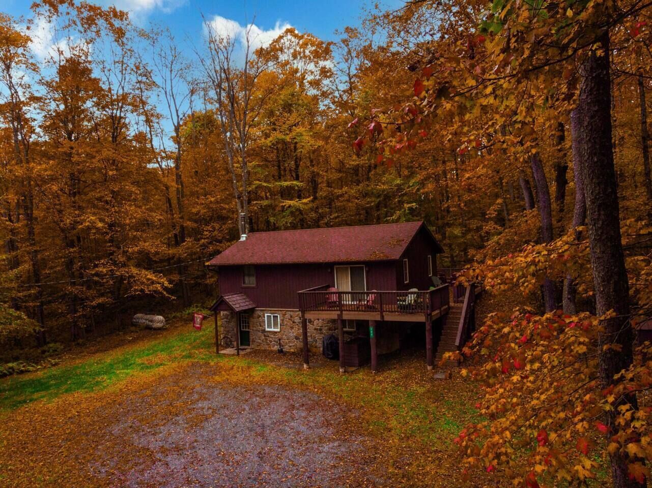 A rustic cabin with a stone foundation, a wooden deck, and a front porch.