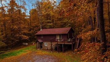 A rustic cabin with a stone foundation, a wooden deck, and a front porch.