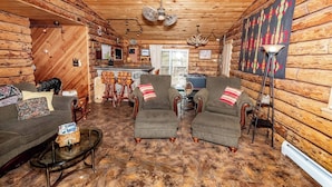 A log cabin interior with a dining area, two armchairs, a sofa, and a coffee table.