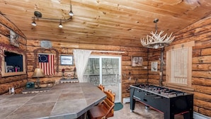 A cozy cabin interior with a stone bar, wooden walls, and a foosball table.