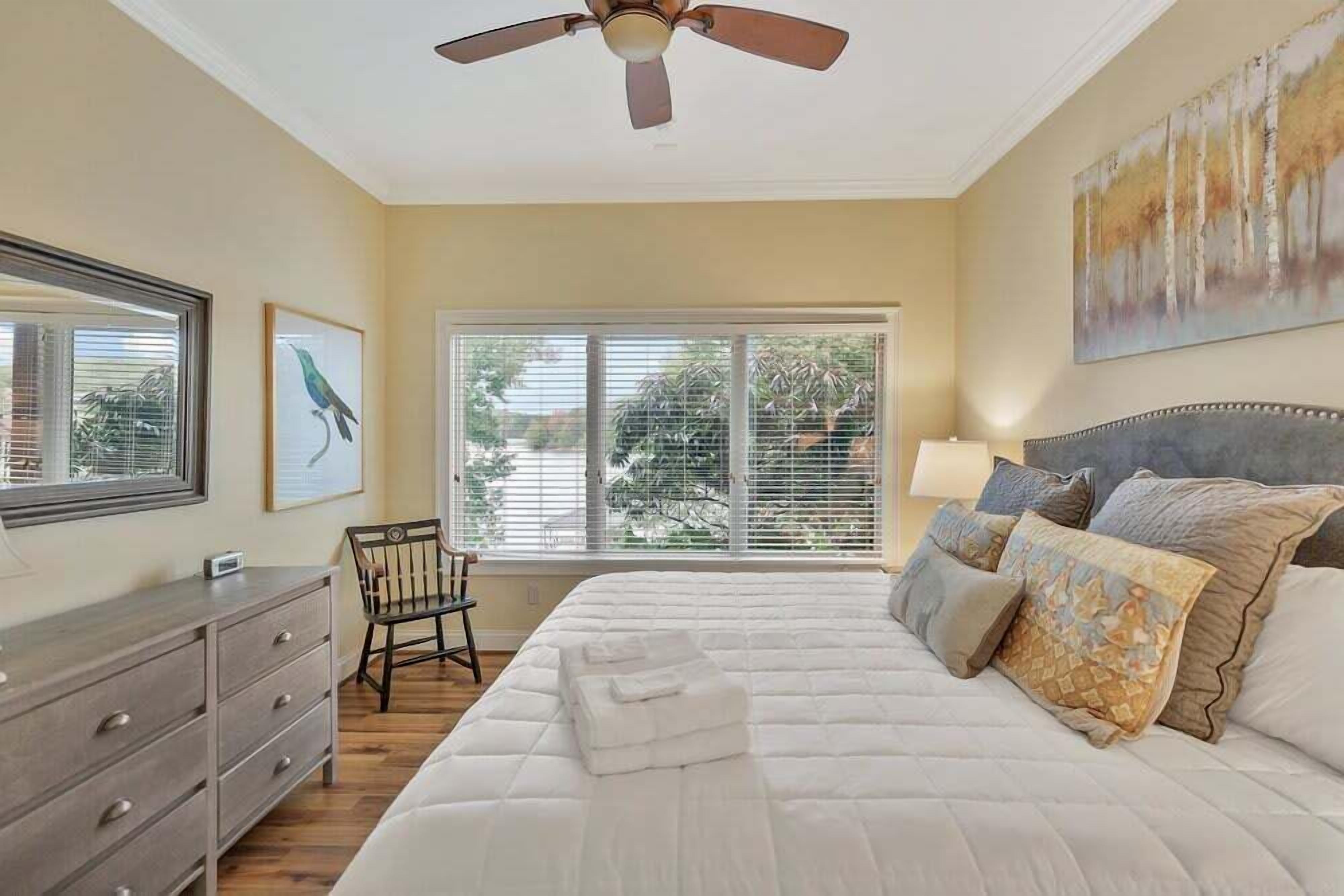 A bedroom with a bed, a chair, a dresser, a ceiling fan, and a window with blinds.