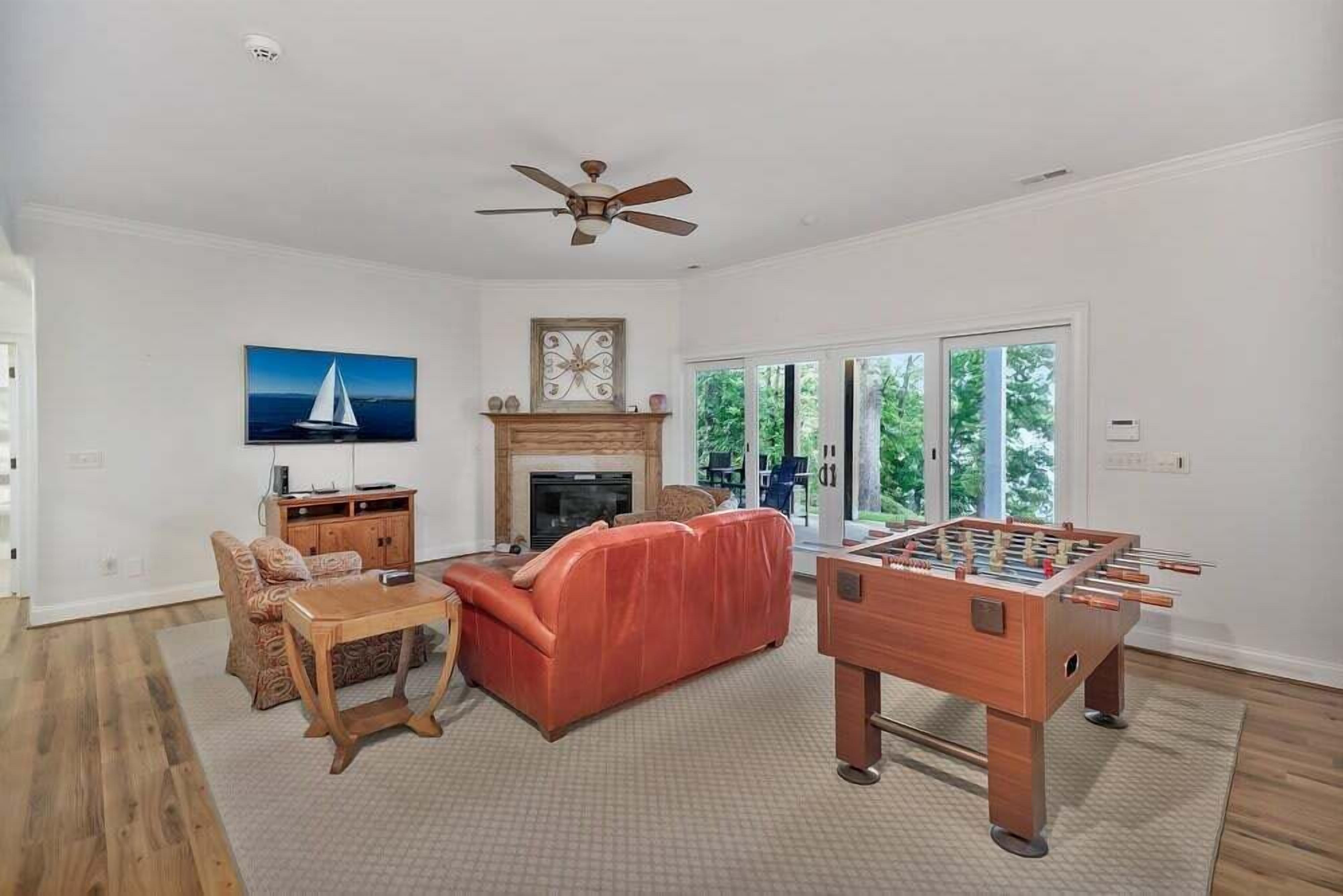 A living room with a fireplace, a sofa, a coffee table, a foosball table, and a ceiling fan.