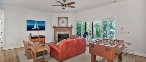 A living room with a fireplace, a sofa, a coffee table, a foosball table, and a ceiling fan.