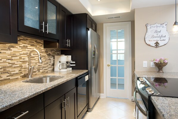 A modern kitchen with dark cabinets, a stainless steel refrigerator, a coffee maker, and a decorative sign on the wall. - Sea-Side Sophistication-3 Story Townhome. Close to Beach. (Hilton Head Island)