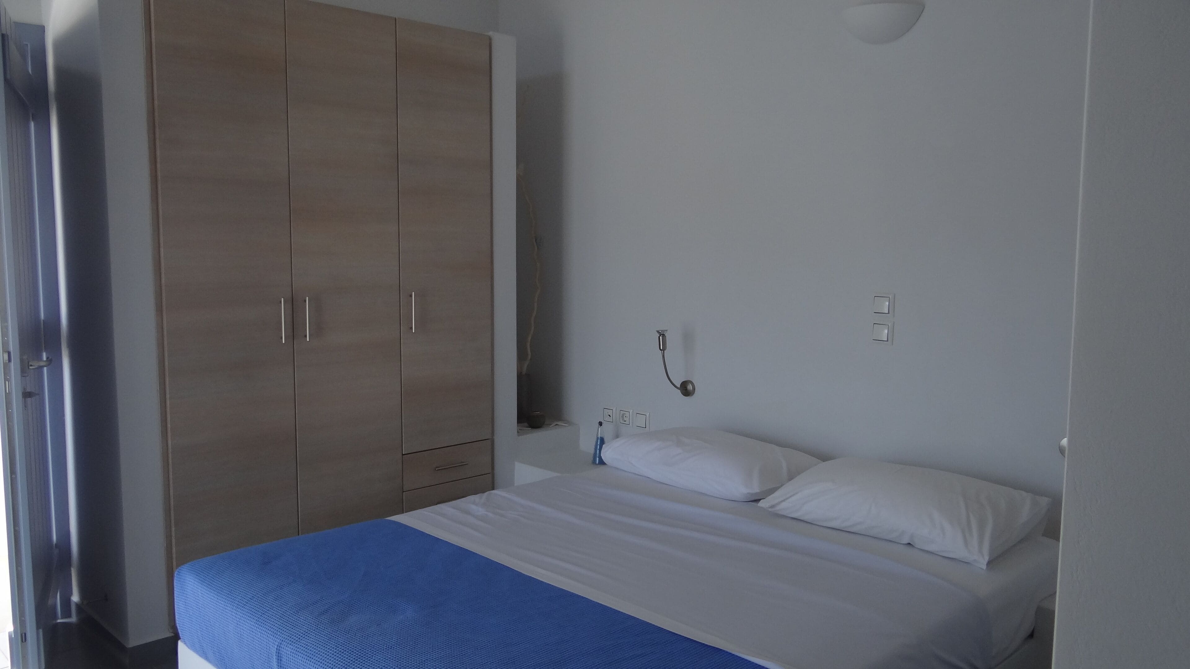 Un dormitorio con una cama, ropa de cama blanca, un armario de madera y un aplique de pared.