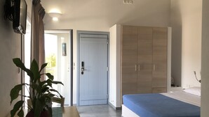 Un dormitorio con cama, armario, escritorio con planta y puerta que da a otra habitación.