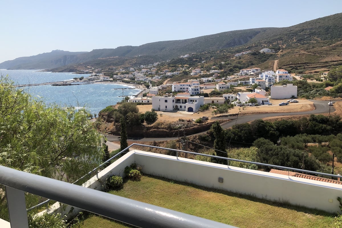 A coastal village with white buildings, a clear blue sea, and hilly terrain.